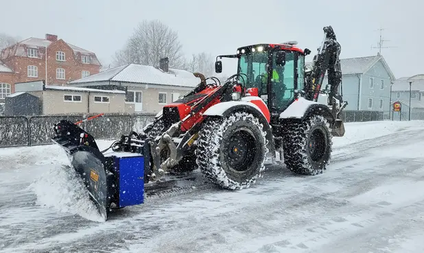 En traktor med plogblad i snöfall. 