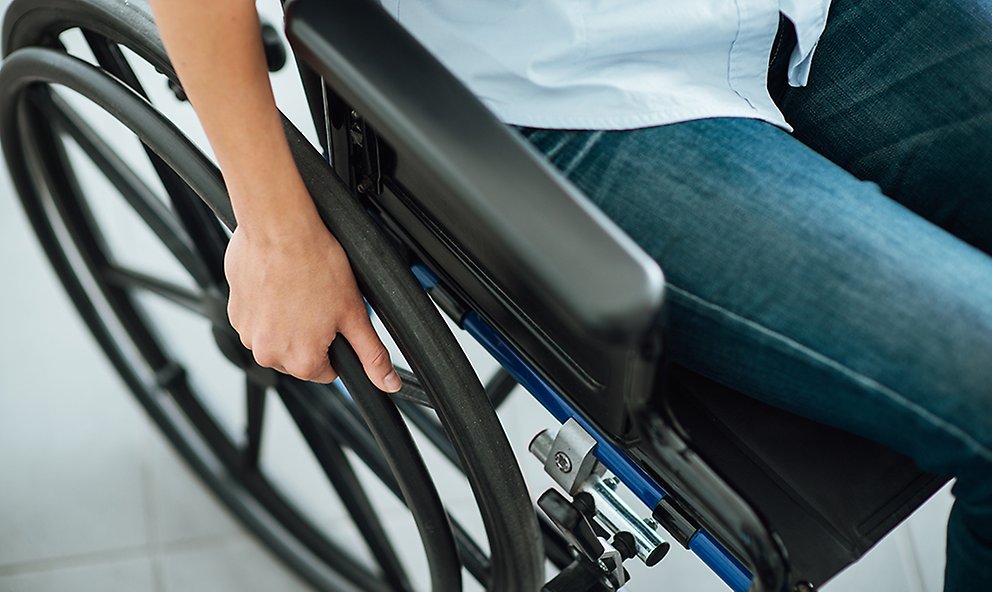 Foto av person i rullstol där ena benet och ena armen samt rullstolens ena hjul och armstöd syns.
