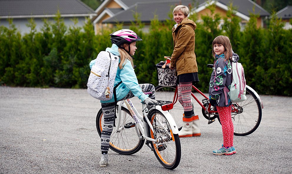 Foto på en vuxen och två barn på cyklar på en gata i ett villaområde.